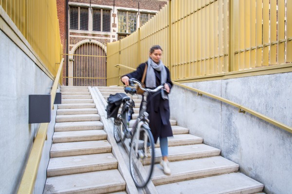 Een fietser gebruikt de fietsgleuf aan de trappen om een fiets in de ondergrondse parking te rijden.