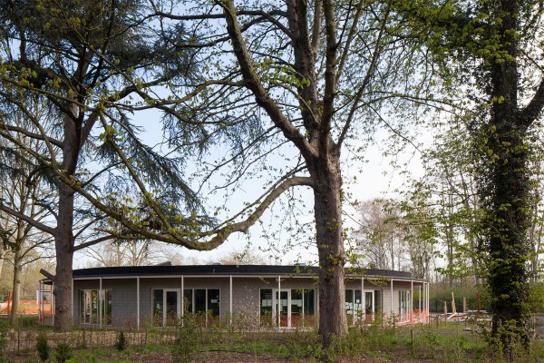 Nieuw rond en laag gebouw voor basisschool Kosmos omgeven door bomen.