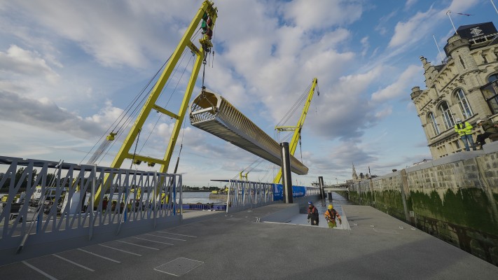 Een van de toegangsbruggen van het ponton van de nieuwe cruiseterminal wordt op haar plek gehesen