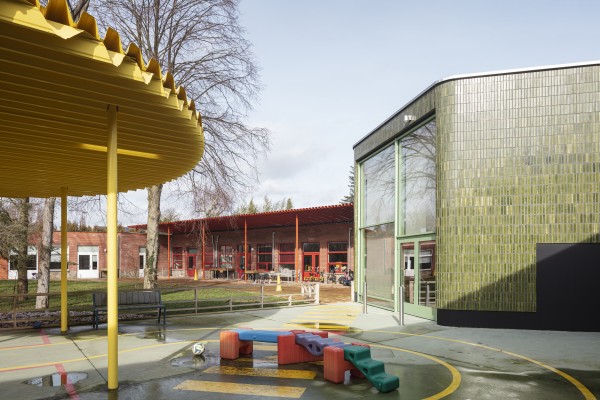 Speelplaats De Leerexpert Dullingen met gele luifel en het groene en rode schoolgebouw op de achtergrond.