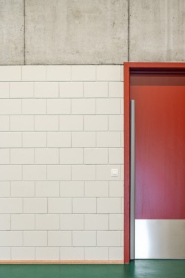 Detail van grijze muur en rode deur met groene sportvloer.