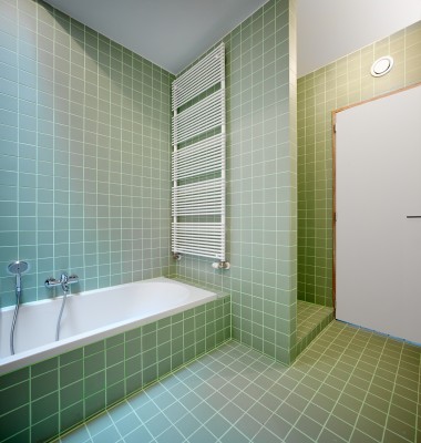 Betegelde badkamer met ligbad, douche en handdoekverwarmer.