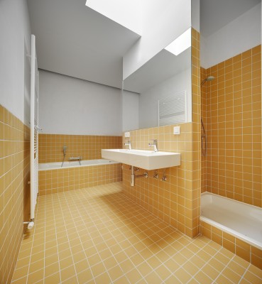 De geel betegelde badkamer is voorzien van ligbad, douche en een wastafel met spiegel.
