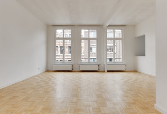 Leefruimte van appartement op eerste verdieping voorzien van mooie parketvloer en 3 grote raampartijen met zicht op straatzijde. Er is een nis voorzien naar de keuken