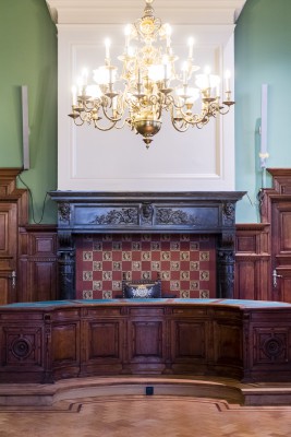 De raadzaal van het districtshuis heeft een parketvloer, een monumentale zwarte marmeren schouw en houten lambrisering.