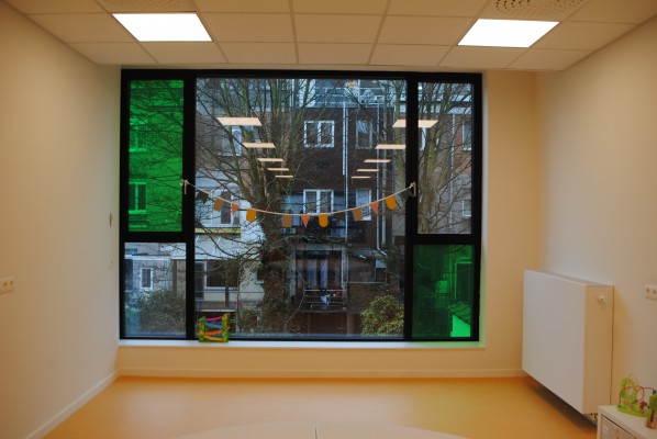 De ruimte komt uit op een groot raam verdeeld in meerdere vakken waarvan het glas bij twee smalle vlakken groen is.