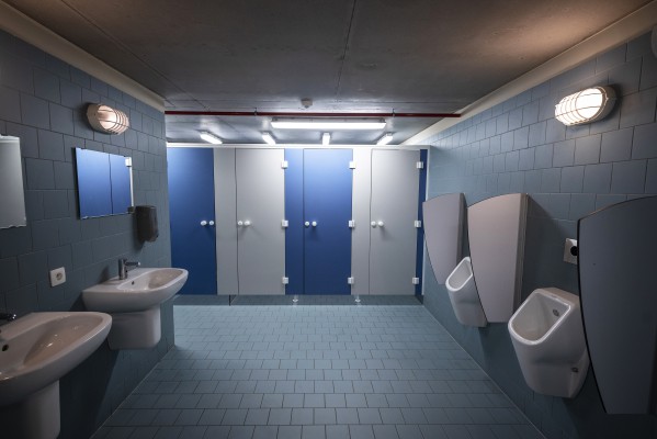 Blauw betegelde ruimte met twee wastafels, twee wandurinoirs en enkele toilethokjes.