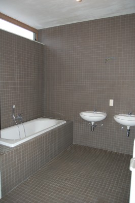 Betegelde badkamer met ligbad en twee wastafels.