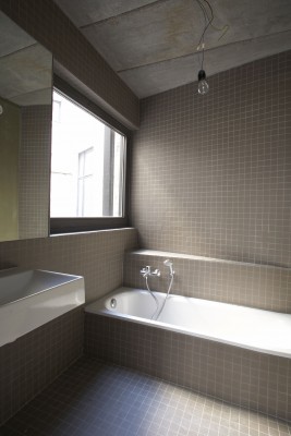 De badkamer is volledig betegeld in donker grijs. Er is een ligbad en lavabo met spiegel geïnstalleerd. Het raam boven het bad zorgt voor natuurlijk licht.