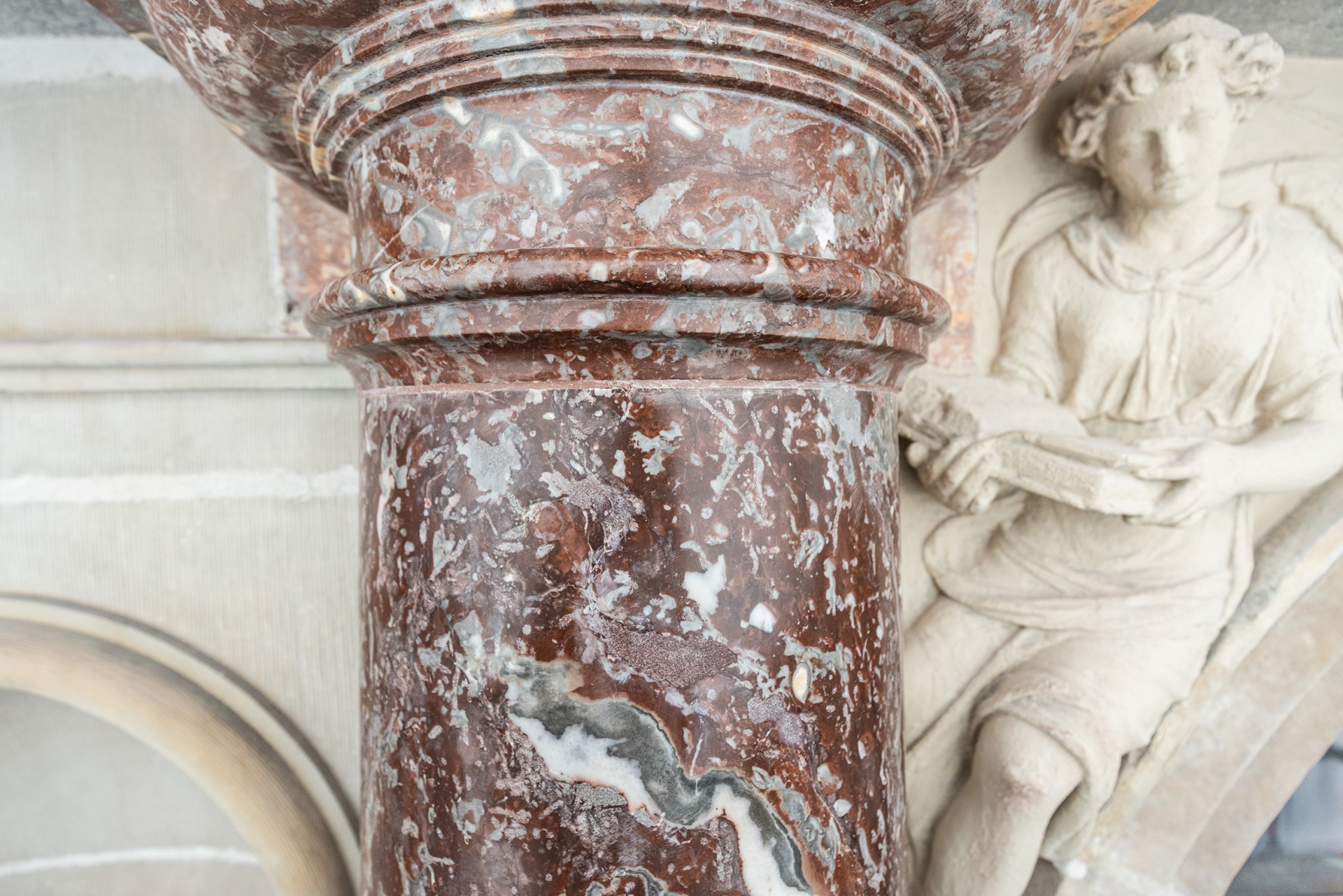 Gerestaureerde rode marmeren zuil met een figuur in witte steen naast.