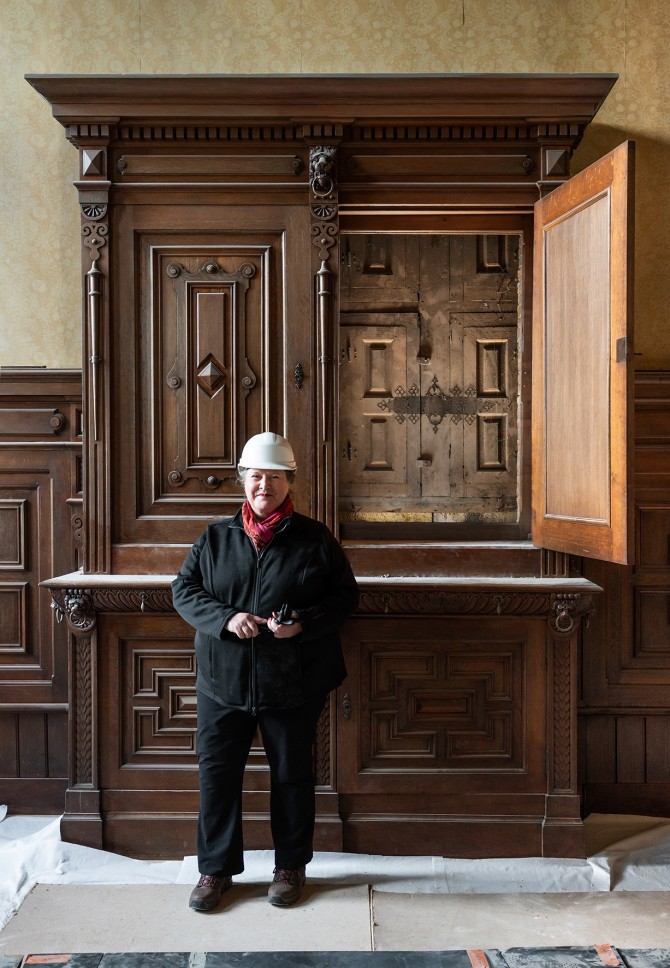 Carola Van den Wijngaert staat voor de houten kast waarachter het 16e-eeuws raam is teruggevonden.