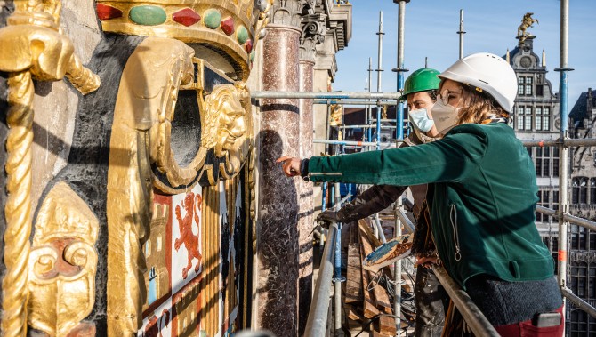 Twee restaurateurs bekijken de grote wapenschilden aan de gevel van het stadhuis.