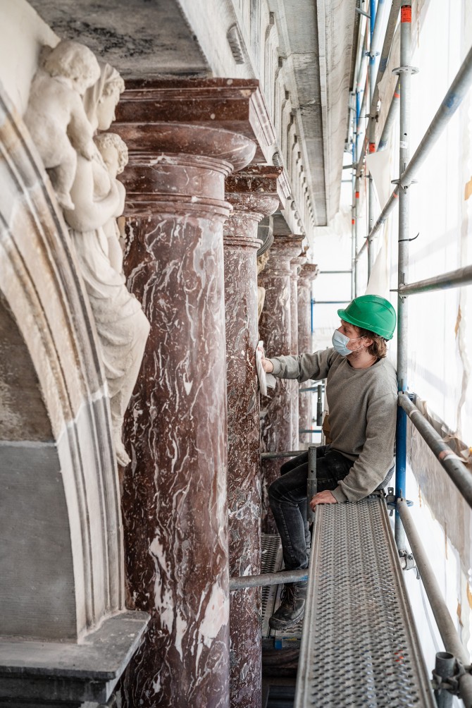 Een restaurateur herstelt de rode marmeren zuilen aan de gevel van het stadhuis