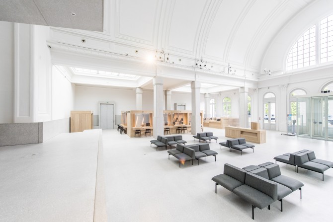 Interieur districtshuis met houten loketten, stoffen banken en veel lichtinval door grote ramen in het vernieuwde gebouw Harmonie. 