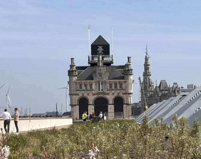 Gebouw op het einde van het verhoogd wandelterras, met op de voorgrond bloembedden