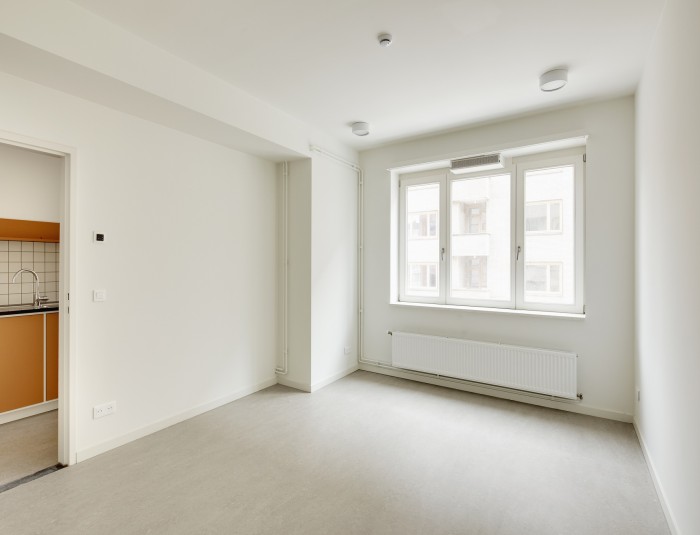 Lege ruimte met groot raam en deuropening naar de keuken.